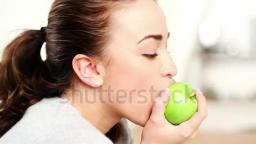 stock-footage-healthy-young-woman-eating-green-apple-and-smiling-at-home-indoors